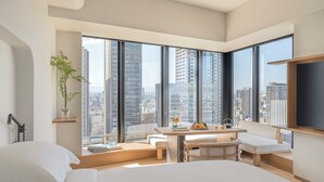 A modern hotel room with a large bed, a dining area, and a view of the cityscape through floor-to-ceiling windows. - Four Seasons Hotel Osaka (Osaka)