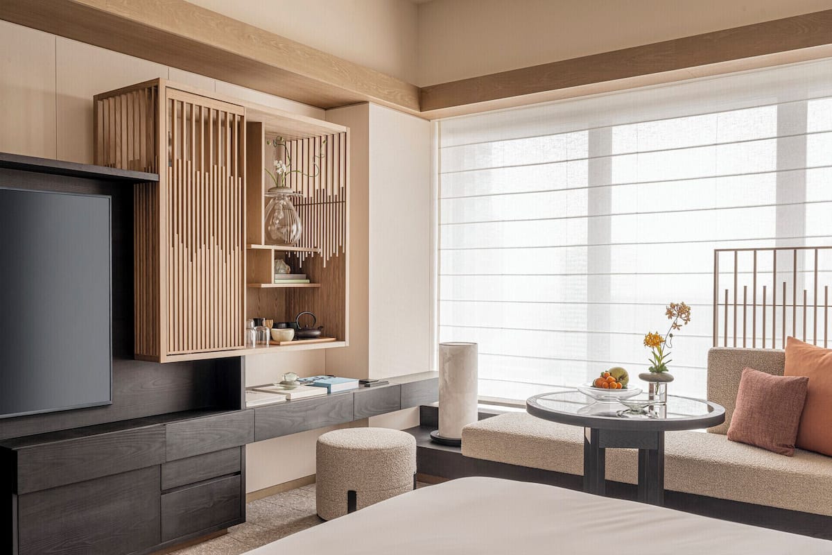 Een moderne hotelkamer met een grote flatscreen televisie, een houten kast met planken, een ronde glazen tafel met een vaas en een bank met kussens.