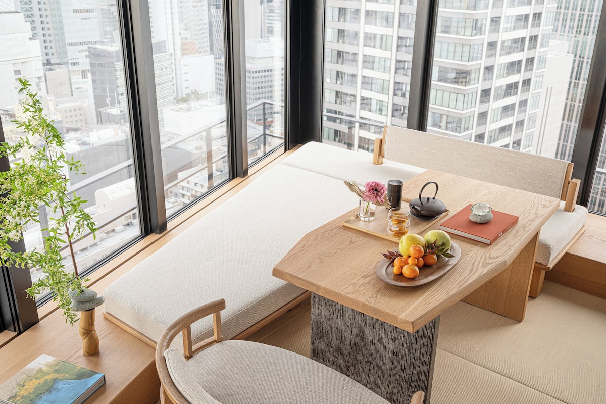 Een moderne eetruimte met een houten tafel, beklede zitplaatsen en uitzicht op een stadsbeeld door grote ramen.