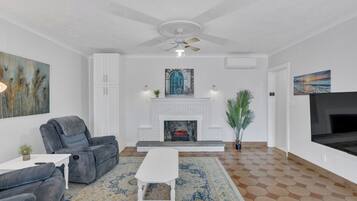 Una sala de estar con chimenea, ventilador de techo y un televisor grande.