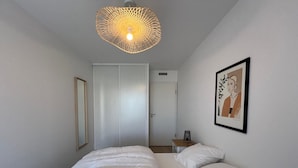 A bedroom with a bed, a bedside table, a lamp, a framed artwork, and a door.