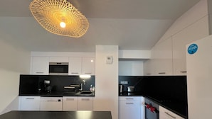 A modern kitchen with white cabinets, black countertops, and a unique pendant light.