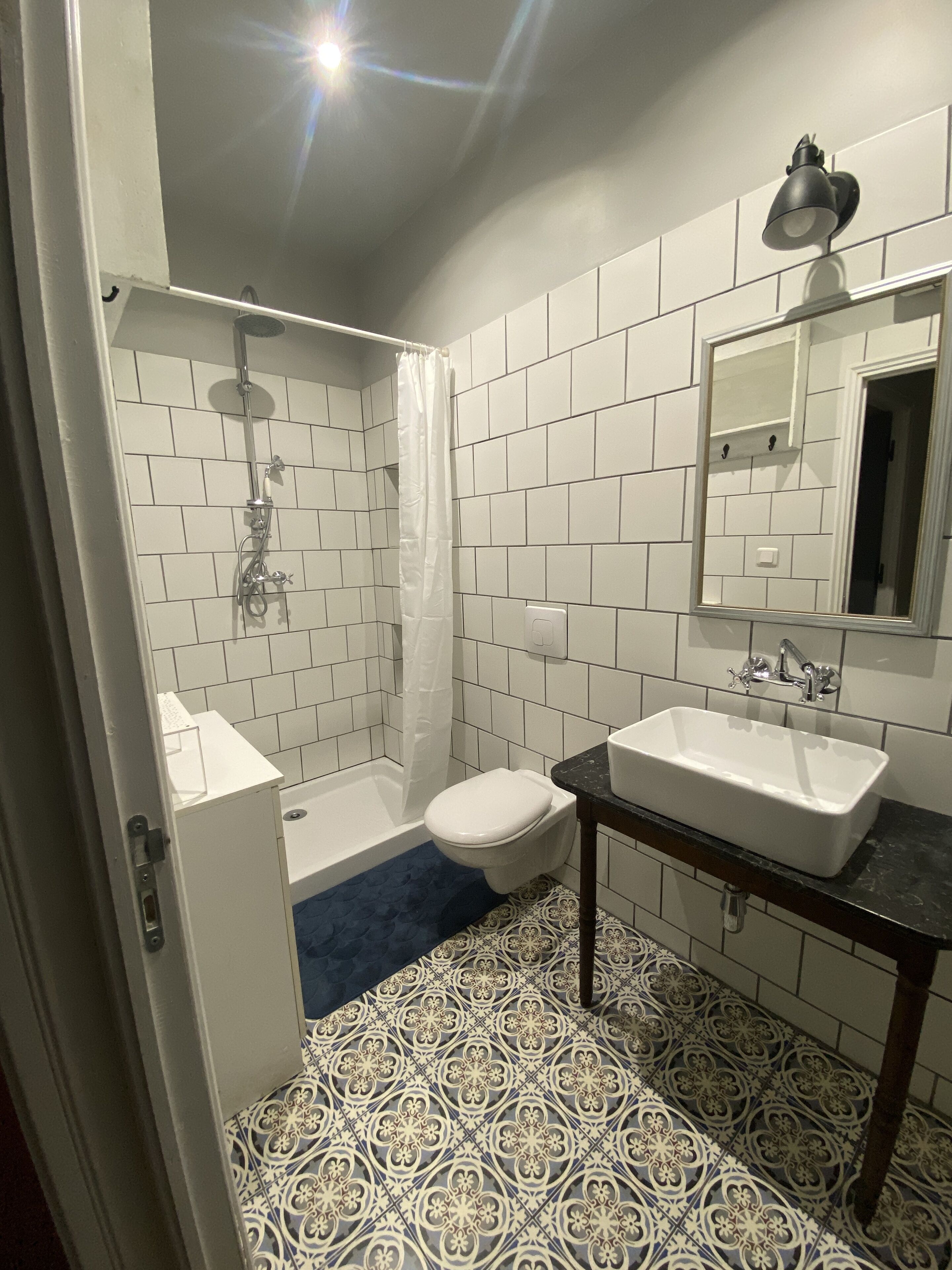 Een badkamer met witte betegelde wanden, een douche, toilet, wastafel en spiegel.