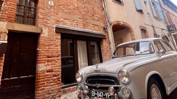 Ein Oldtimer vor einem Backsteinhaus mit Kopfsteinpflasterstraße.