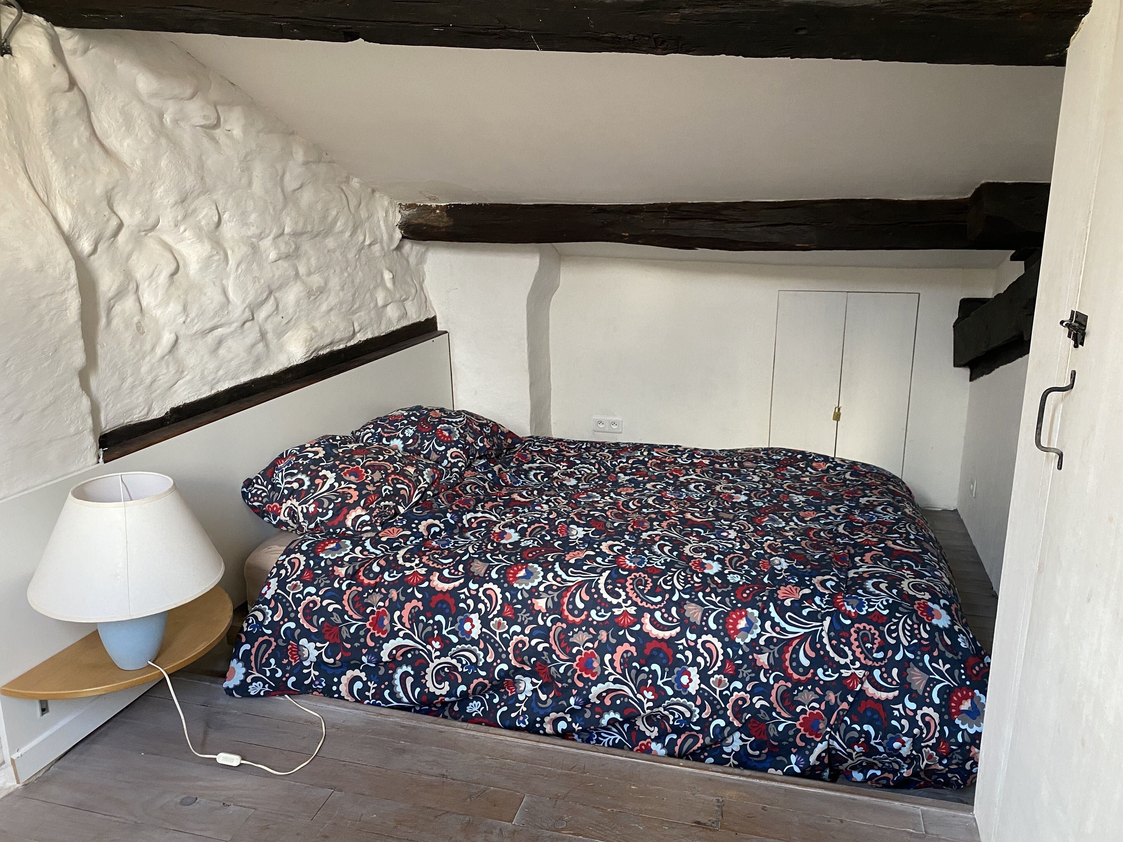 Ein kleiner, gemütlicher Raum mit einem Bett, einer Lampe und einem Holzregal.