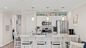 Una cucina moderna con mobili bianchi, elettrodomestici in acciaio inossidabile e illuminazione a sospensione.