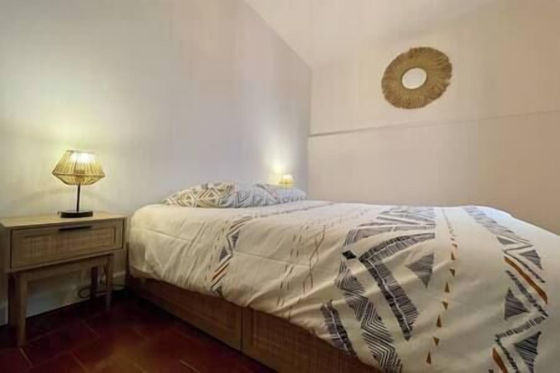 A bedroom with a bed, bedside tables, and a wall-mounted light fixture.