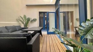 En moderne udendørs terrasse med træterrasse, sort fletmøbler og plantekasser.