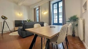Et spiseområde med et træbord og stole, en sofa, en gulvlampe og en potteplante.