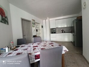 Et moderne køkken med lyse skabe, et rustfrit stål køleskab og et spiseområde med et bord dækket til fire personer.