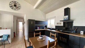 A modern kitchen with dark cabinetry, a wooden dining table with blue chairs, and a large wall clock.