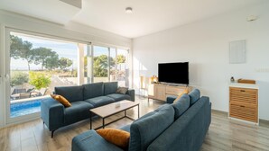 Ein modernes Wohnzimmer mit einer großen Sofagarnitur, einem Flachbildfernseher und Blick auf einen Pool und Bäume.