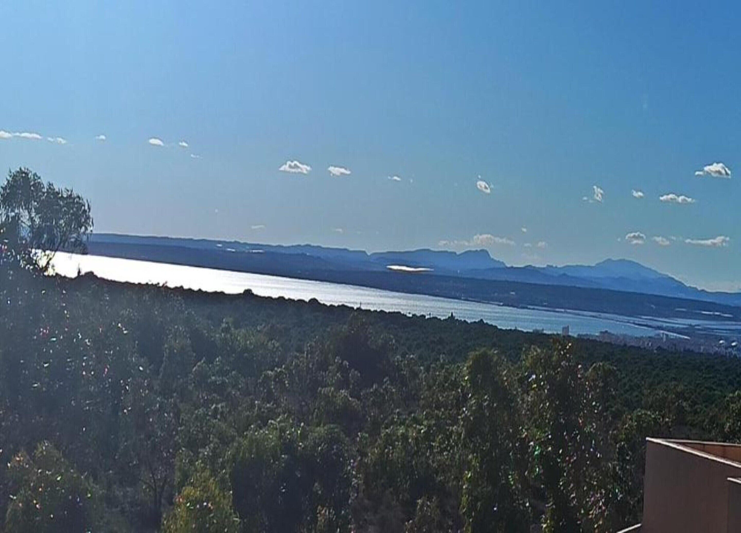 Paesaggio costiero con vista sul mare e montagne in lontananza.