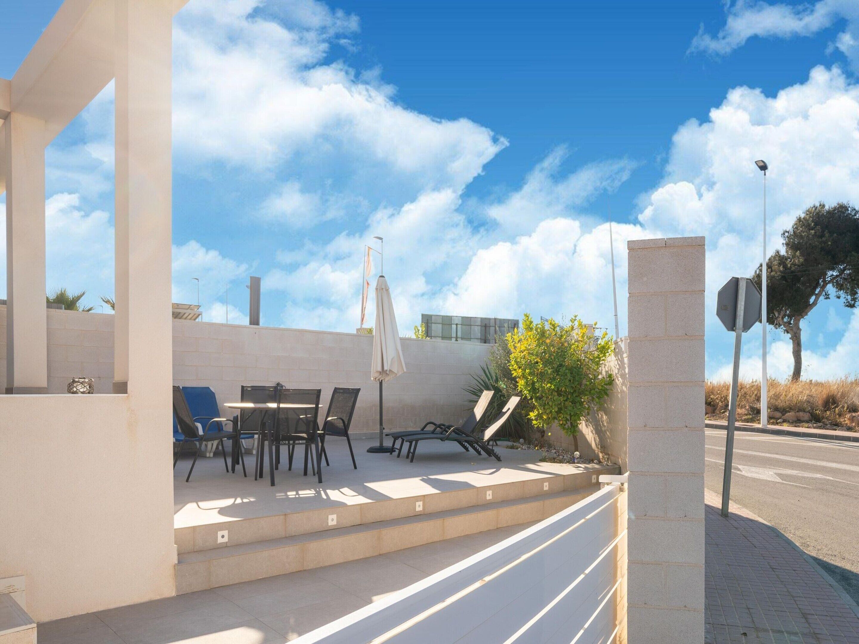 An outdoor seating area with tables and chairs, a white umbrella, and a stone pillar.