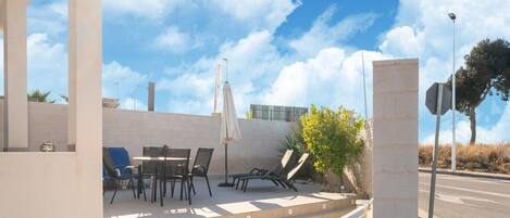 An outdoor seating area with tables and chairs, a white umbrella, and a stone pillar.