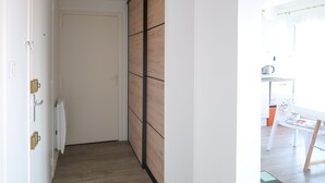 Un passadís estret amb una porta corredissa de fusta i una porta blanca. Es veuen una cadira blanca i una taula petita a l'habitació propera.