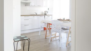 Cuina moderna amb armaris blancs, taulell de fusta i zona de menjador amb caires blancs i taula de vidre.