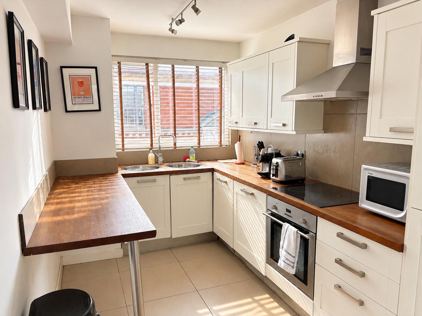 A modern kitchen with white cabinets, a wooden countertop, a built-in oven, and a window with blinds.