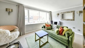 A modern living room with a green sofa, a white fur chair, a small black table, and a large window with curtains. - The Elden - No.17 (London)