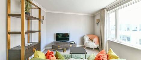 Una sala de estar con un sofá verde, una estantería de madera, un televisor y un sillón.