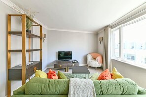 A living room with a green sofa, a wooden bookshelf, a television, and a chair.