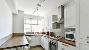A modern kitchen with white cabinets, a wooden countertop, a built-in oven, and a microwave. - The Elden - No.17 (London)