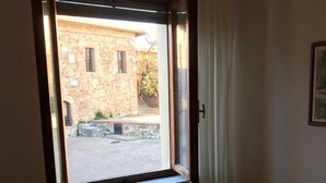 Une pièce avec une fenêtre donnant sur une cour, un canapé avec une télécommande et un tableau accroché au mur.