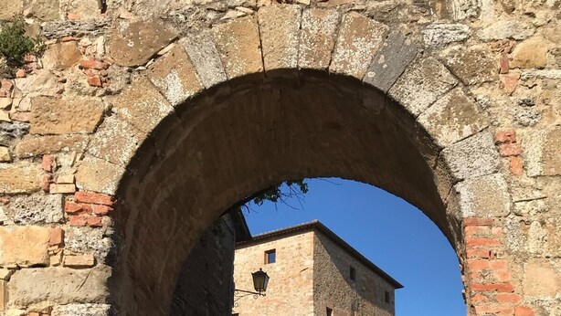 Un portail en pierre en forme d’arc donnant accès à un bâtiment dont le sol est recouvert de carreaux.