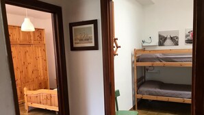 Une chambre avec un lit superposé, une armoire en bois, une chaise verte et un tableau encadré au mur.