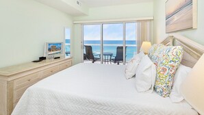 A hotel room with a large bed, a desk with a computer, and a view of the ocean through the sliding doors.