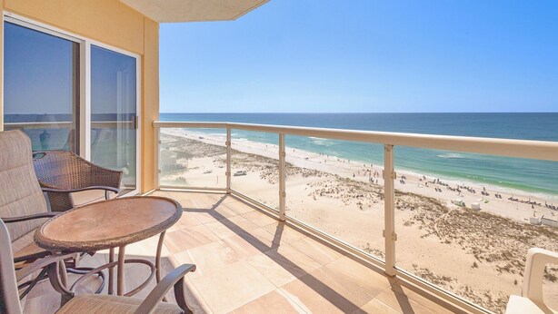 A balcony with a view of a beach, furnished with chairs and a table.
