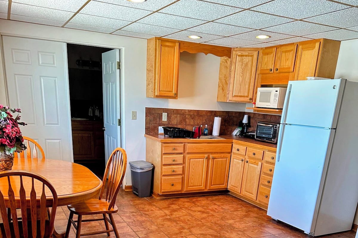 A kitchen with wooden cabinets, a white refrigerator, a microwave, and a dining table with chairs.