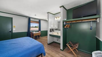 A room with a bed, a desk, a chair, a bathroom with a sink and mirror, and a television mounted on the wall.