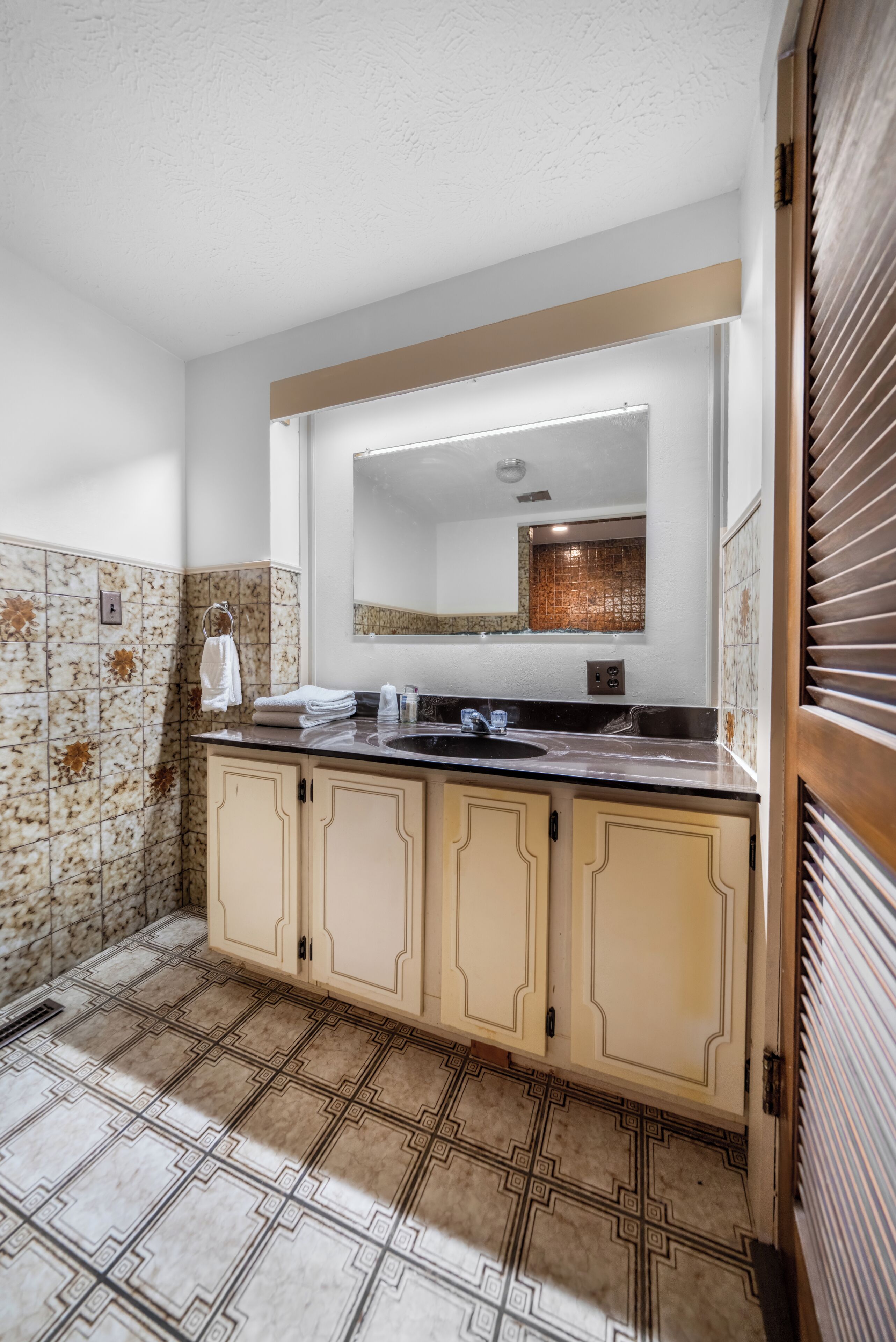A bathroom with a large mirror, a sink, and a tiled floor.
