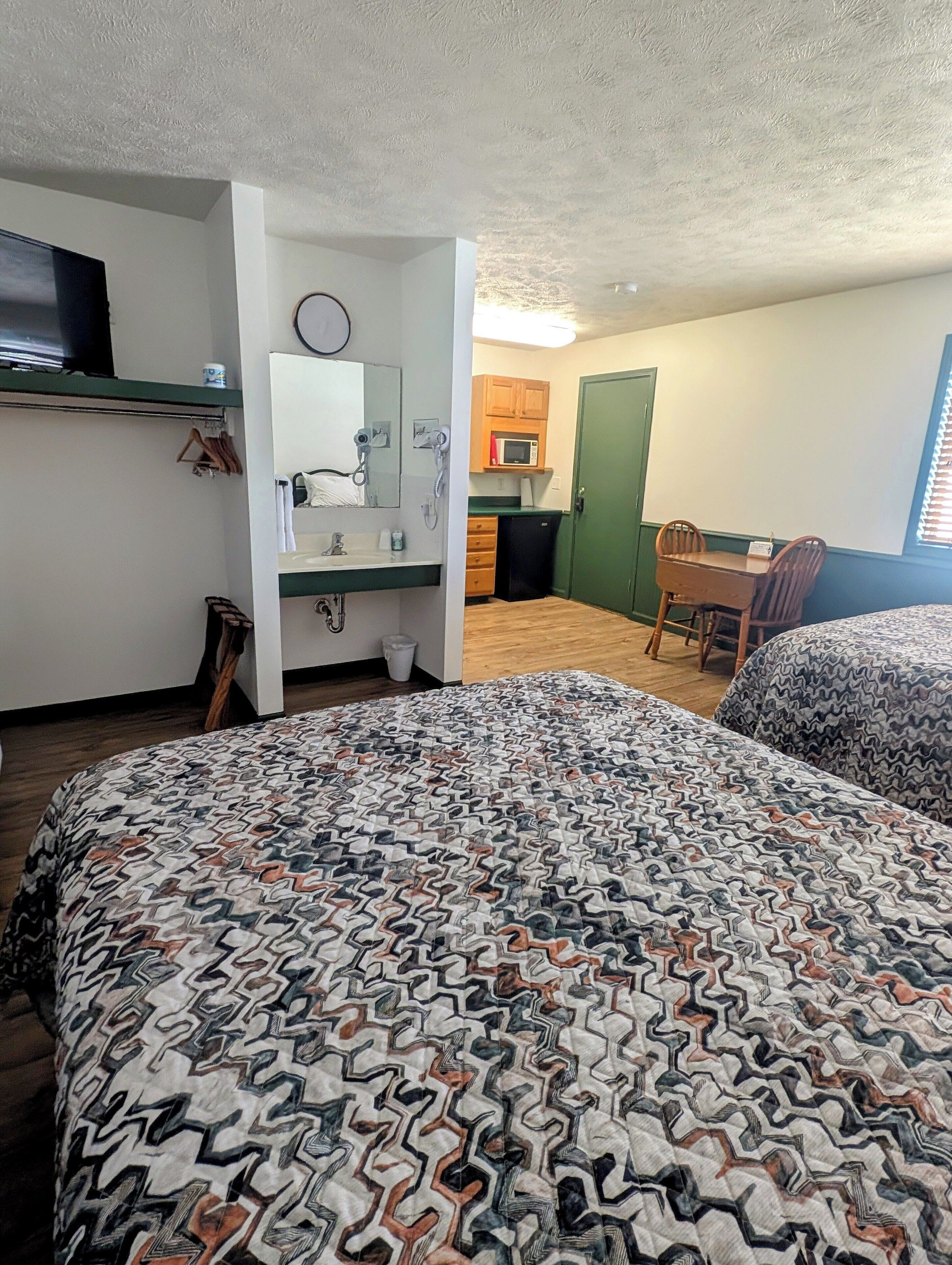 A room with a bed, a desk, a chair, a microwave, and a small kitchenette.