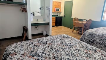 A room with a bed, a desk, a chair, a microwave, and a small kitchenette.