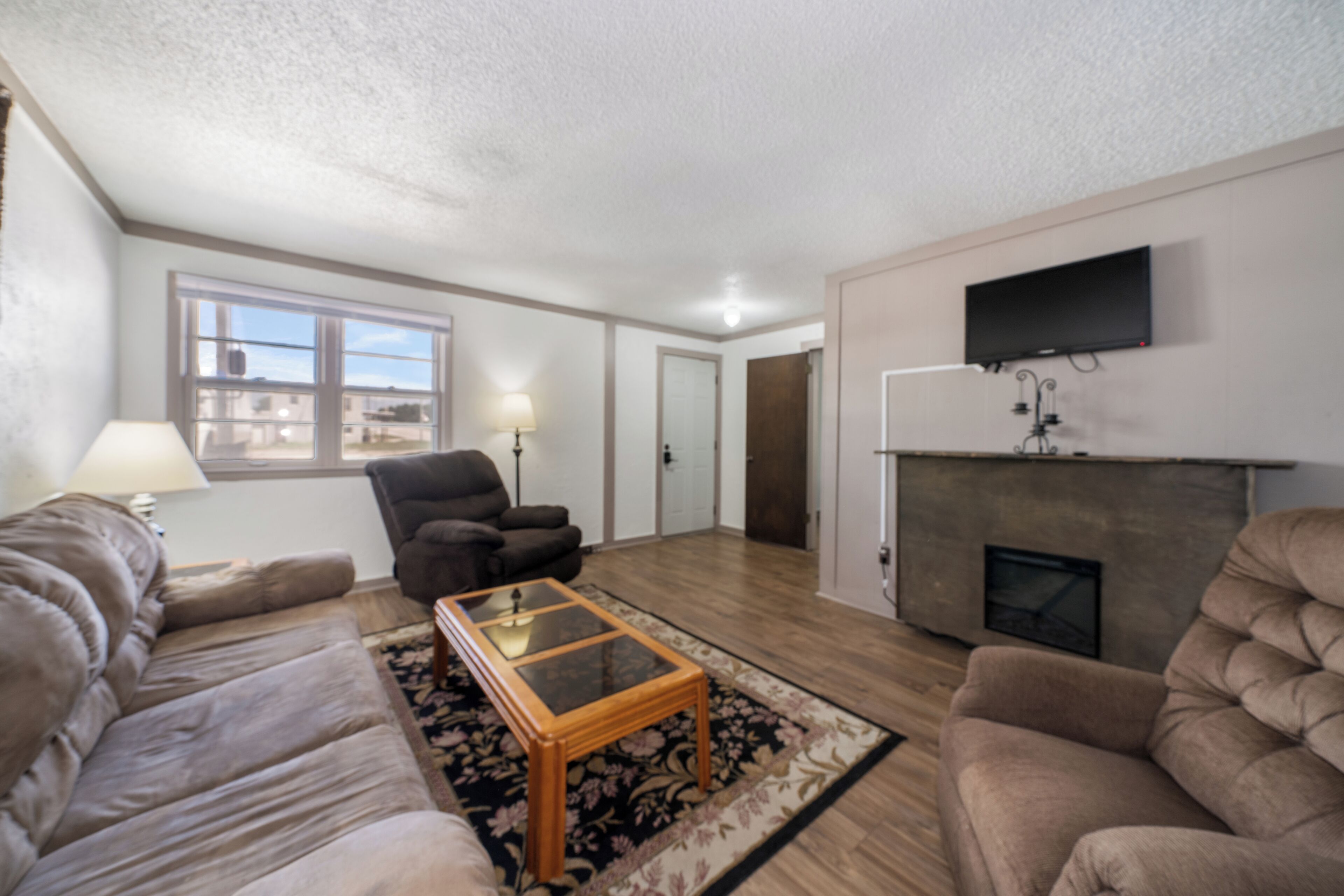 A living room with a sofa, armchair, and a coffee table. There is a fireplace and a TV mounted on the wall.