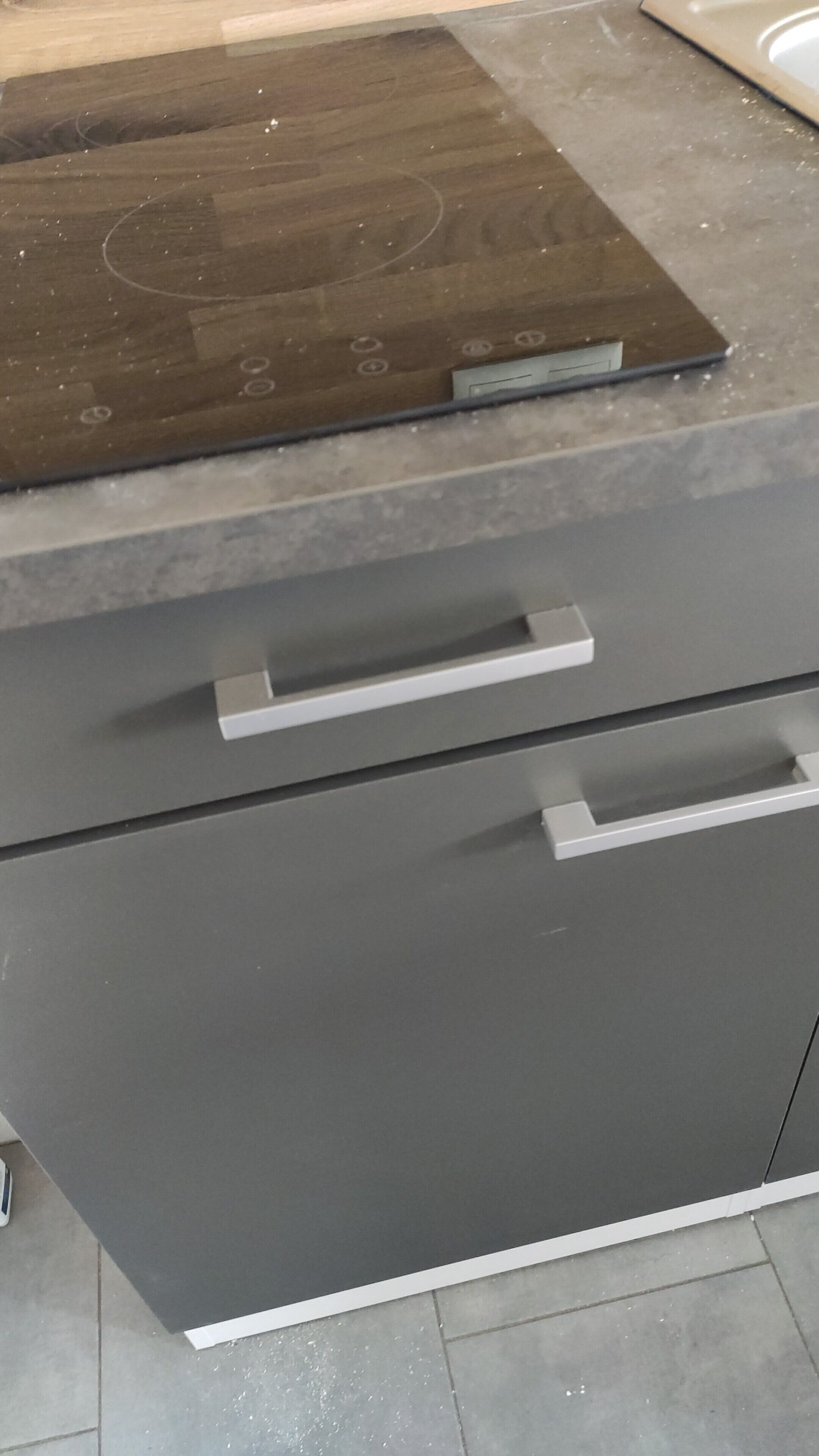 Eine Küche mit dunkler Arbeitsplatte, einem eingebauten Ofen und einem grauen Schrank mit zwei Schubladen und einem Griff.