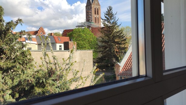 A view from a window overlooking a church with a clock tower, surrounded by trees and buildings. - Alstadt kiek mal wedder in  (Wismar)