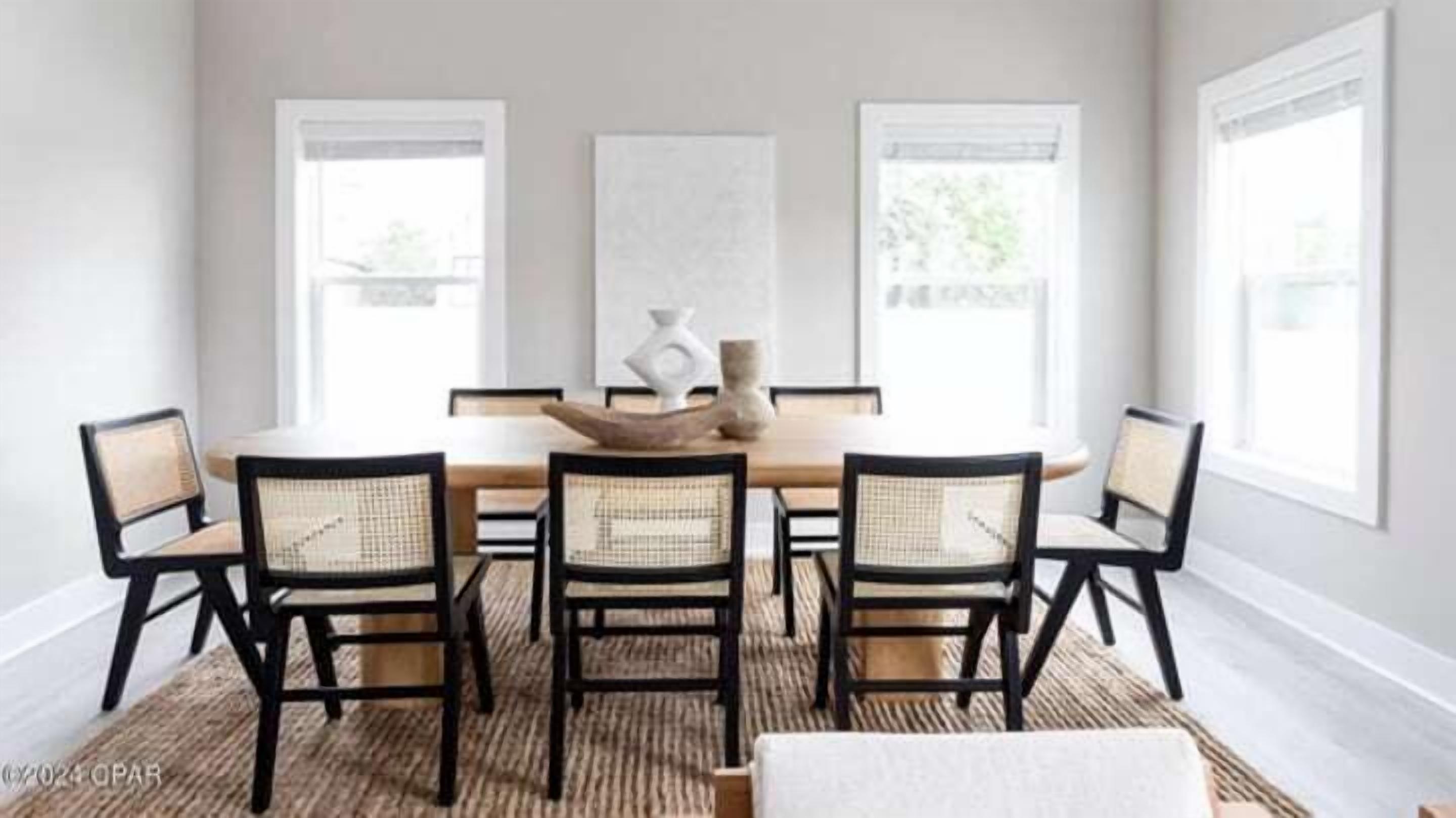 Un coin repas avec une table en bois et six chaises, de grandes fenêtres et un tapis au sol.