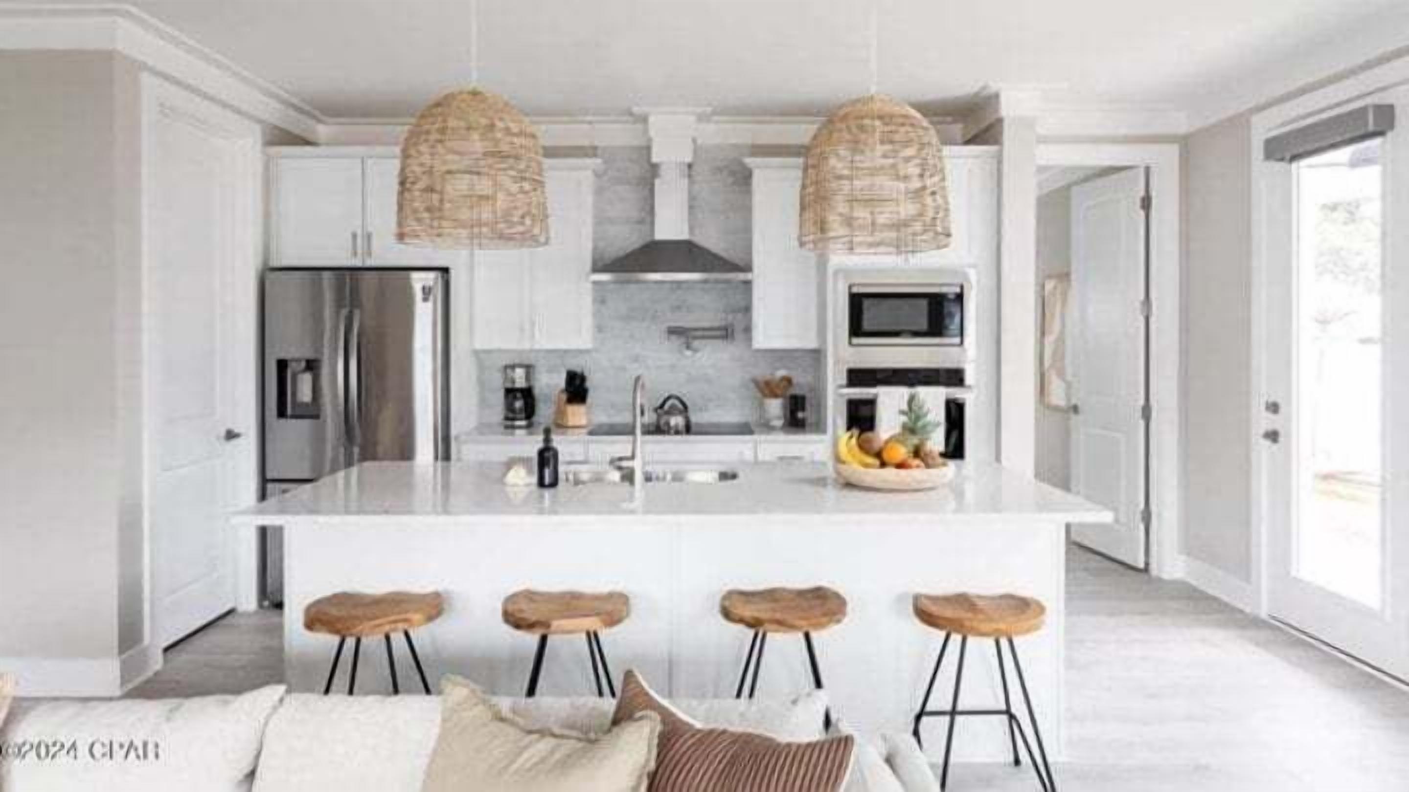Une cuisine moderne dotée d’un îlot central, de tabourets de bar, de luminaires suspendus et offrant une vue sur l’extérieur.