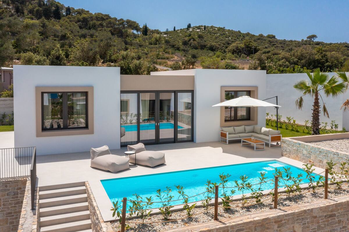 Ein moderner Poolbereich im Freien mit einem klaren, blauen Pool, weißer Gartenmöbel und Blick auf einen Hügelhang.
