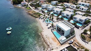 An aerial view of a coastal resort with modern villas, a beach, and clear blue waters. - The Palms Resort (Tkon)