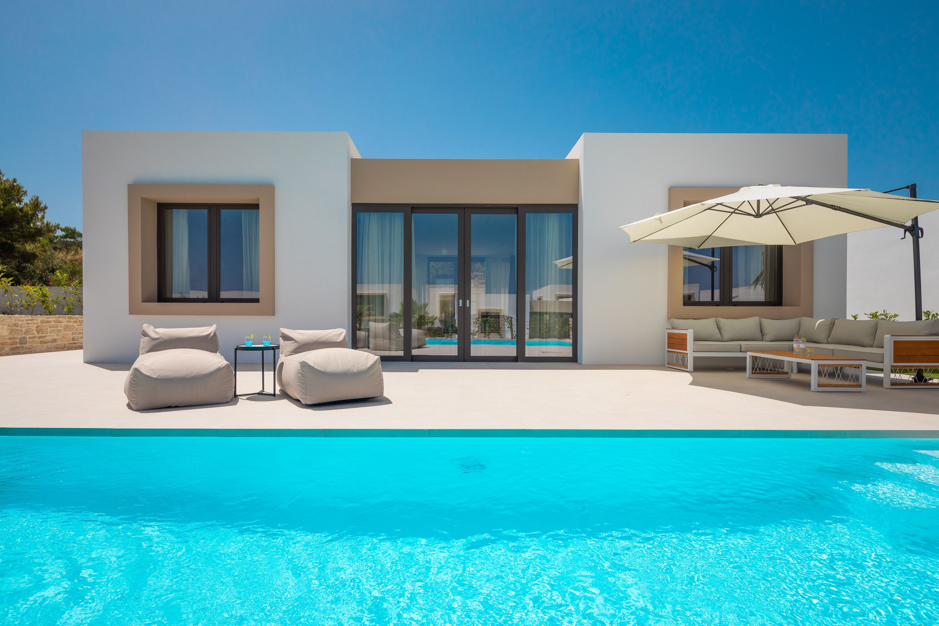 A modern house with a swimming pool, outdoor seating, and a large umbrella.