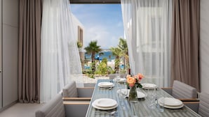 A dining area with a table set for four, overlooking a beach and palm trees. - The Palms Resort (Tkon)