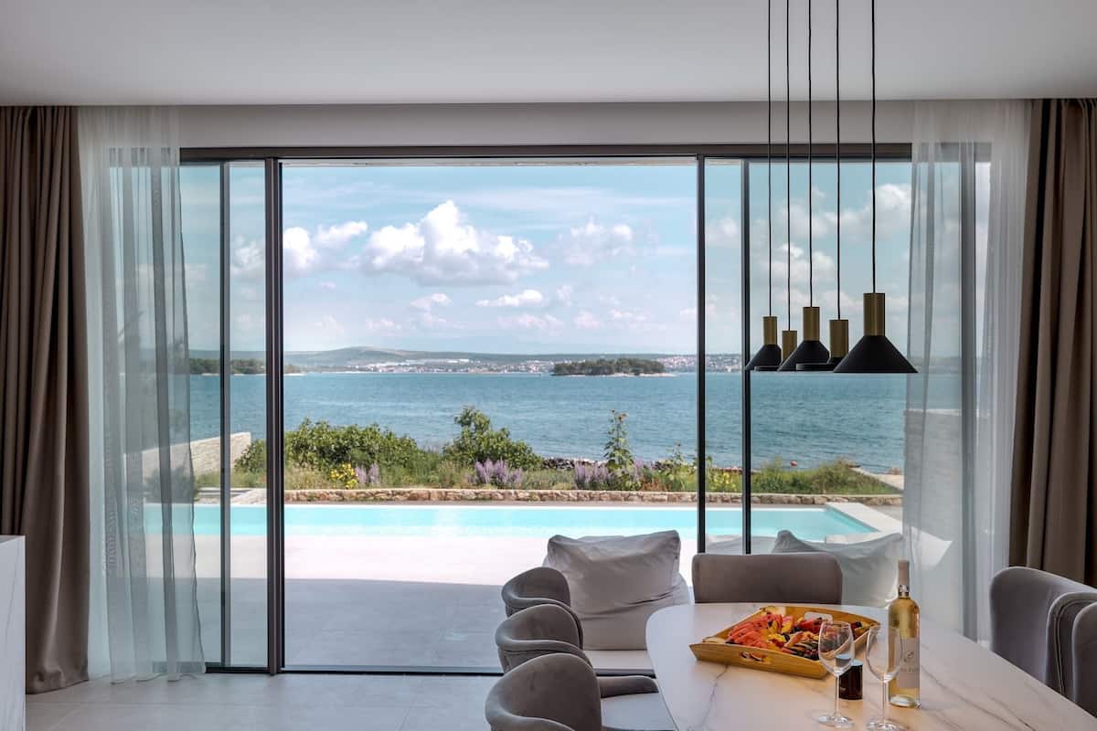 Ein modernes Zimmer mit einer großen Schiebeglasdoor zum Pool und Blick aufs Meer.