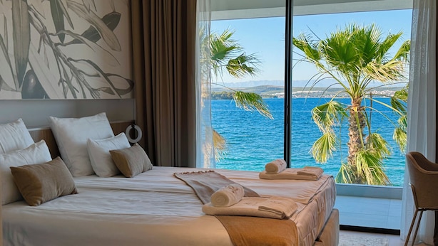 A bedroom with a large bed, a view of the sea, and a palm tree. - The Palms Resort (Tkon)
