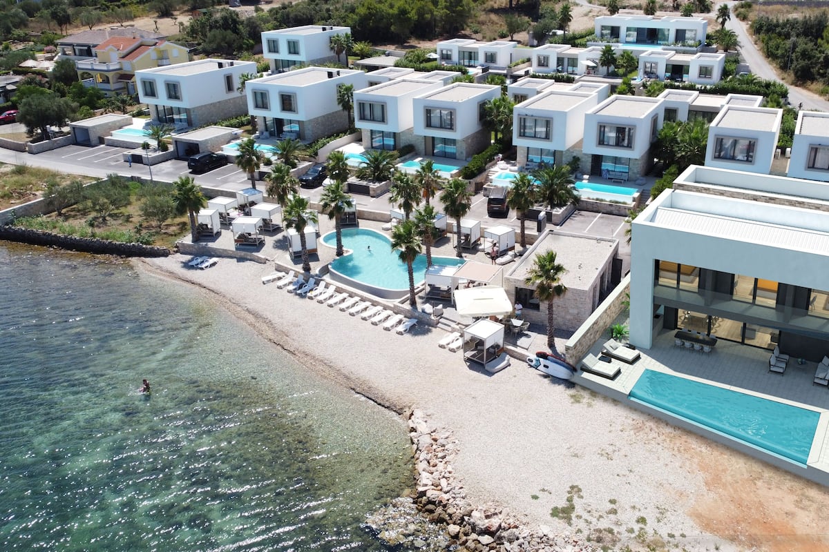 Ein modernes Resort mit mehreren Villen, einem zentralen Pool und einer Strandlage.