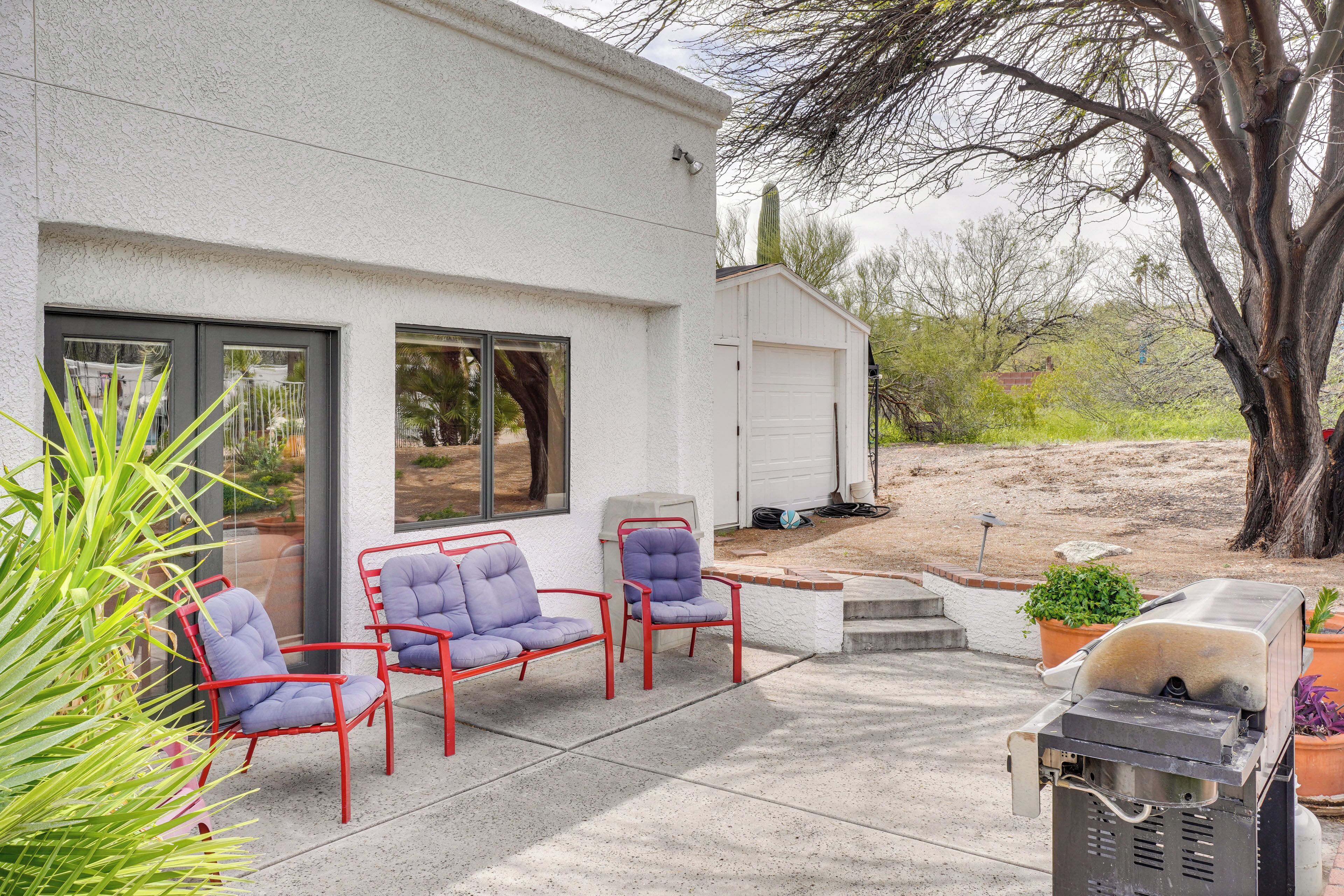 A patio with red metal chairs and a barbecue grill.
