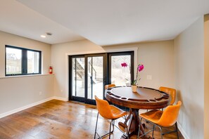 A dining area with a round table and four orange chairs, a potted plant, and a view through a glass door.